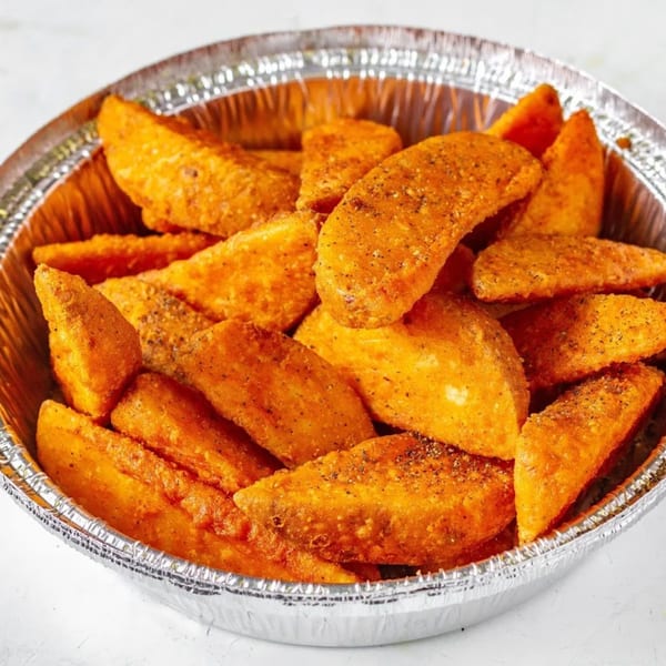 A foil container filled with golden-brown, seasoned potato wedges from Mikie's Pizza & Subs.