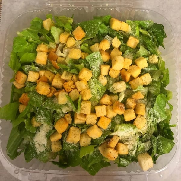 A Caesar salad from Mikie's Pizza & Subs, with crisp romaine, croutons, and grated cheese in a plastic container.