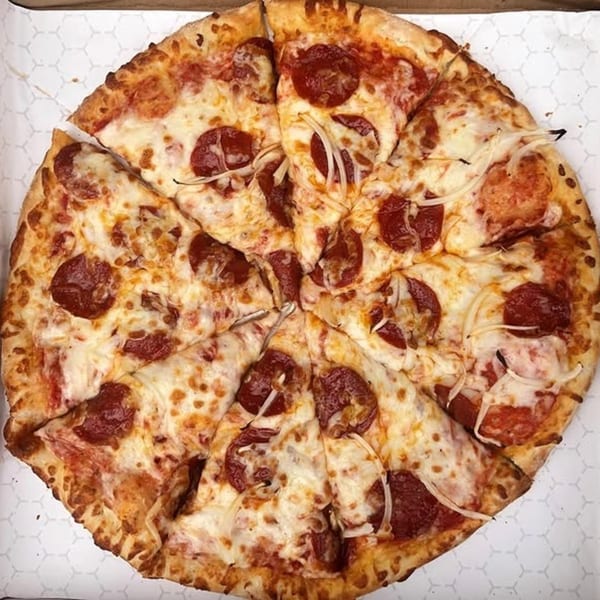 A whole pepperoni and onion pizza, sliced into eight pieces, in a white delivery box.
