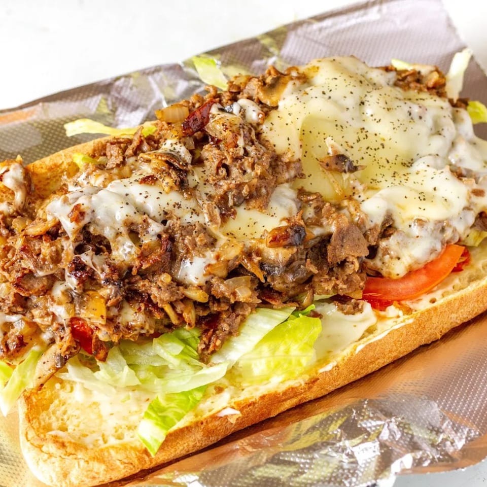 A Mikie's Pizza & Subs cheesesteak with melted cheese, meat, lettuce, and tomatoes on a sub roll.
