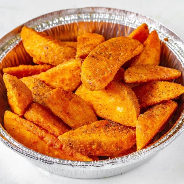 Seasoned potato wedges, golden brown and crispy, served in a foil container.