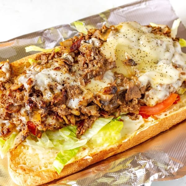 A Mikie's Pizza & Subs cheesesteak sub with melted cheese, steak, onions, lettuce, and tomatoes.
