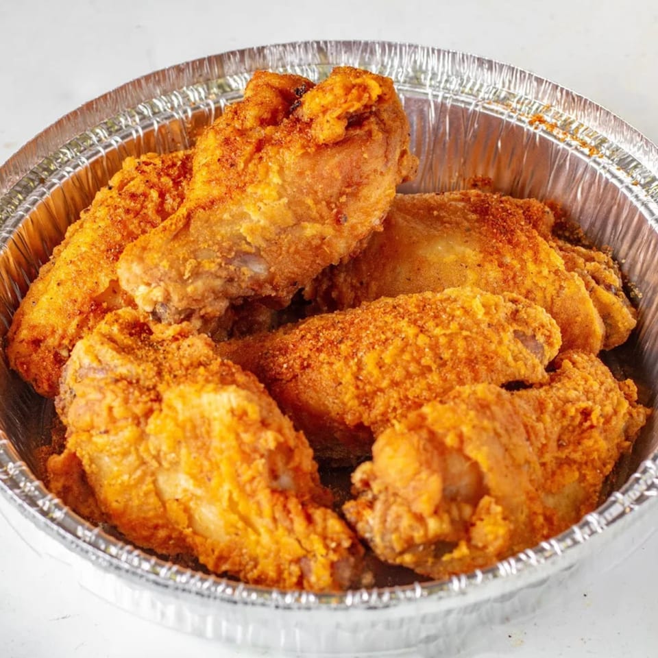 Crispy, golden-brown chicken wings, seasoned with spices, served in a round aluminum foil container.