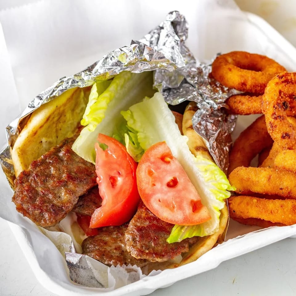 Mikie's Pizza & Subs gyro with meat, lettuce, and tomatoes, served with onion rings.