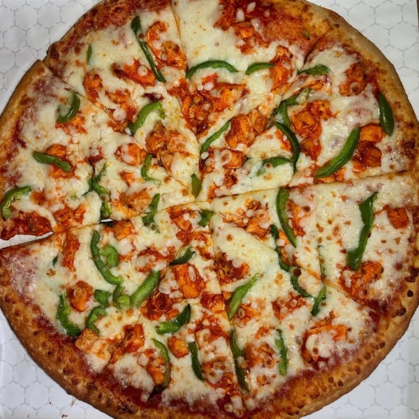 A Mikie's Pizza & Subs buffalo chicken pizza with green peppers, cut into slices.